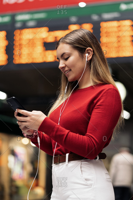 Attractive young woman listening to music wearing headphones and looking at her phone at a train station
