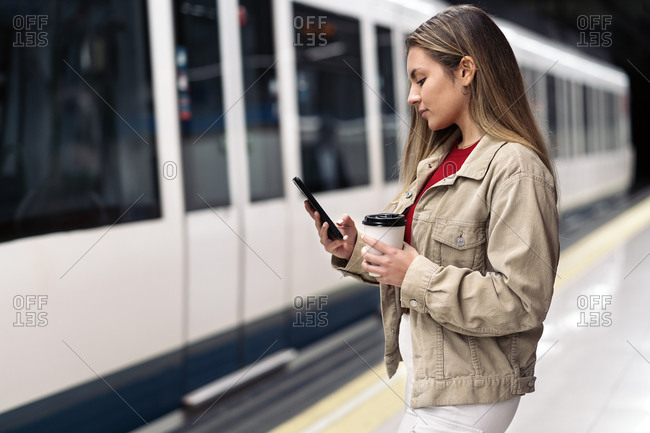 Pretty young woman standing in the train platform holding a cup of coffee