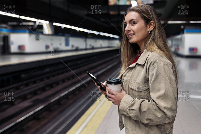 Pretty young woman waiting in the train platform using her phone