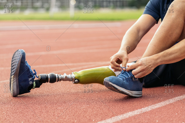 Close up disabled male athlete with leg prosthesis tying his shoe on a running track