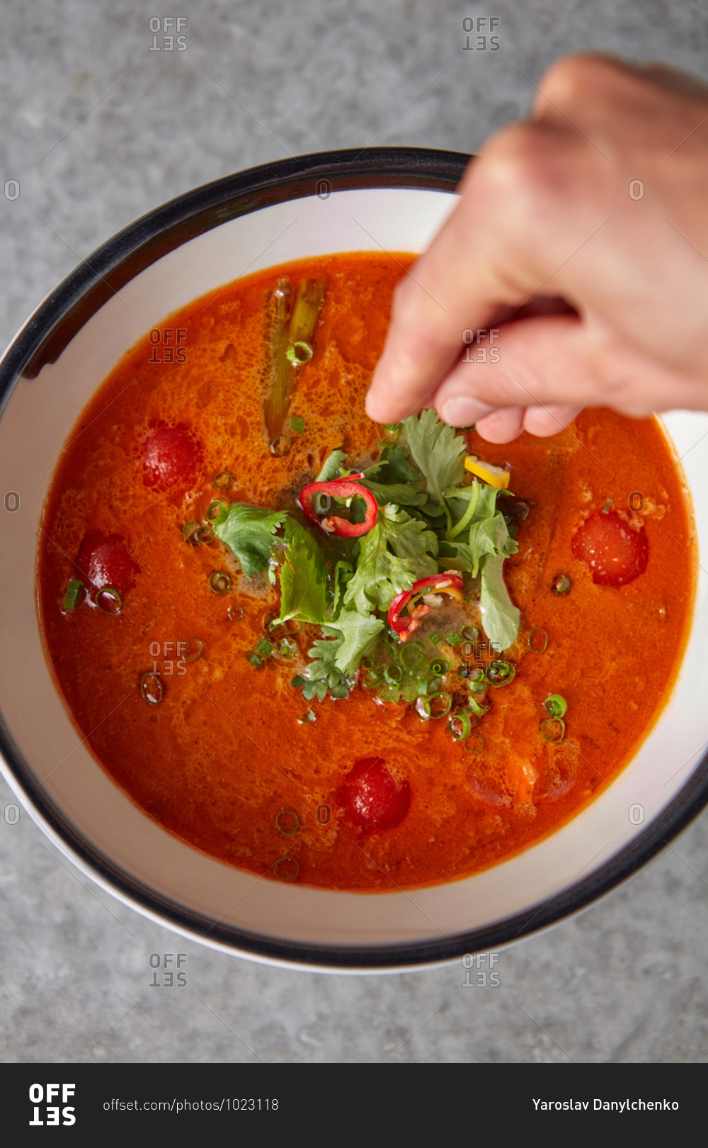 Woman hand above bowl of red spicy vegetable soup.