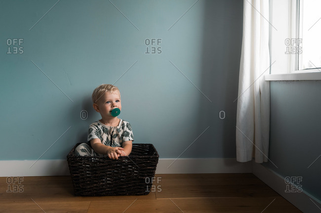 Toddler boy sitting in basket by window