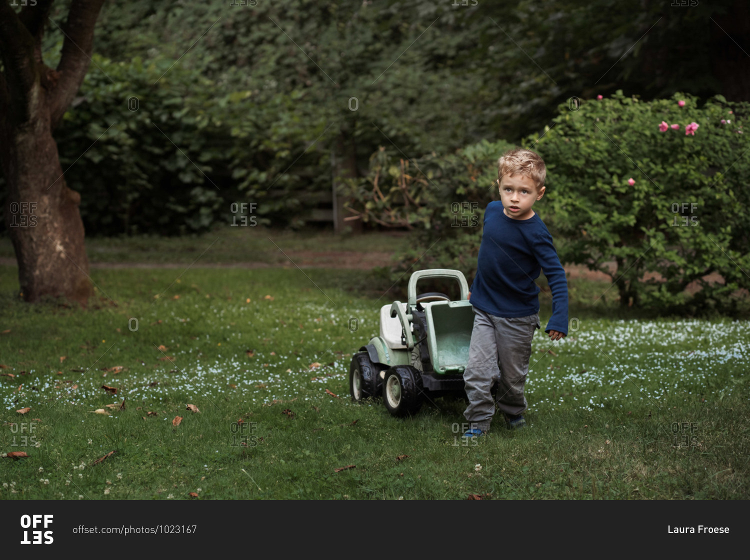 Child pulling a ride-on tractor through the yard