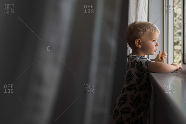 Toddler boy standing by window eating a snack