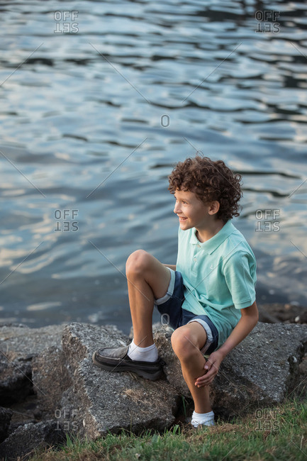 Curly haired boy sitting on large rocks on the coast of British Columbia, Canada