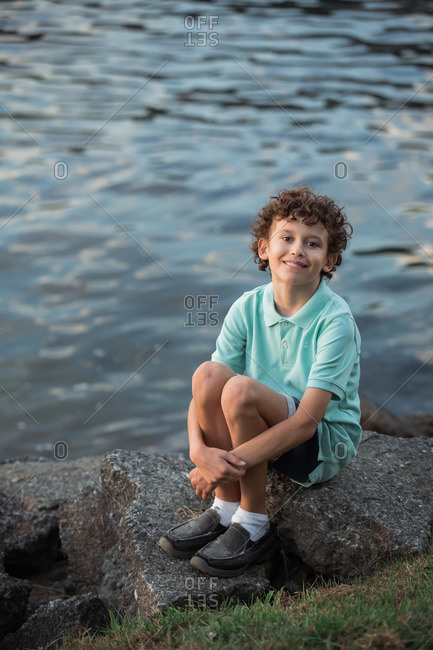 Portrait of a curly haired boy sitting on large rocks on the coast of British Columbia, Canada