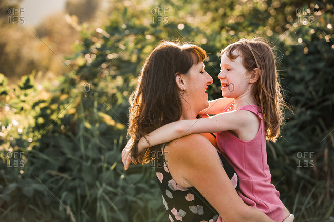 Mother hugging young daughter in a field at sunset