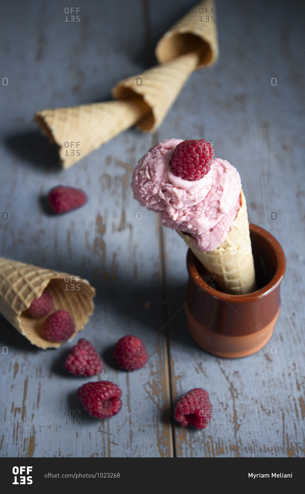 Raspberry ice cream in a waffle cone with fresh raspberries on a rustic wooden surface