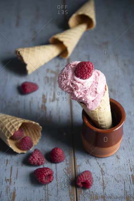 Raspberry ice cream in a waffle cone with fresh raspberries on a rustic wooden surface