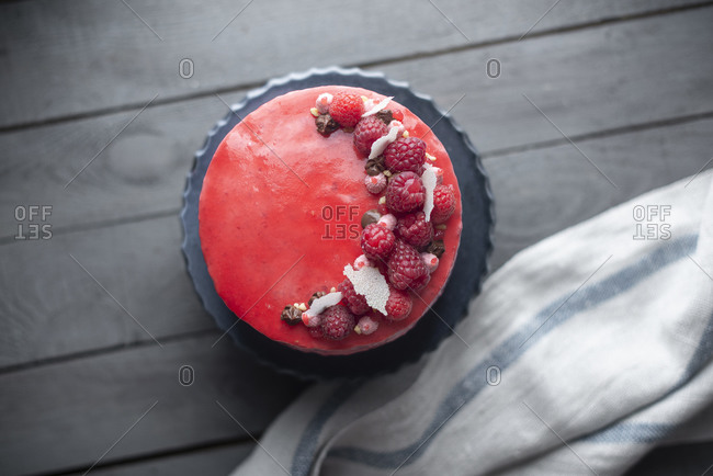 Overhead view of a red glazed raspberry layer cake on a wooden table