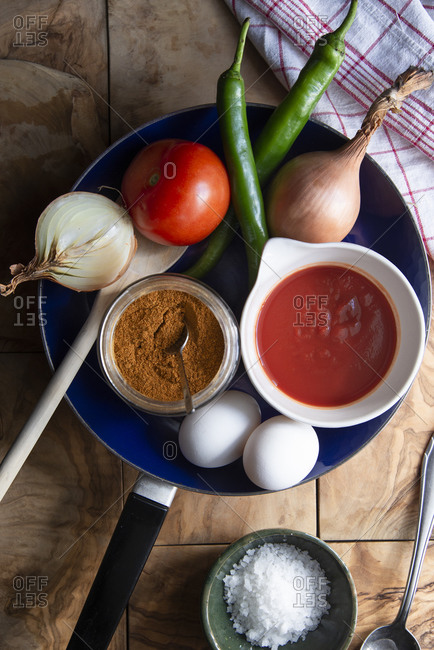 Overhead view of ingredients of a Tunisian shakshuka in a pan on a wooden backdrop