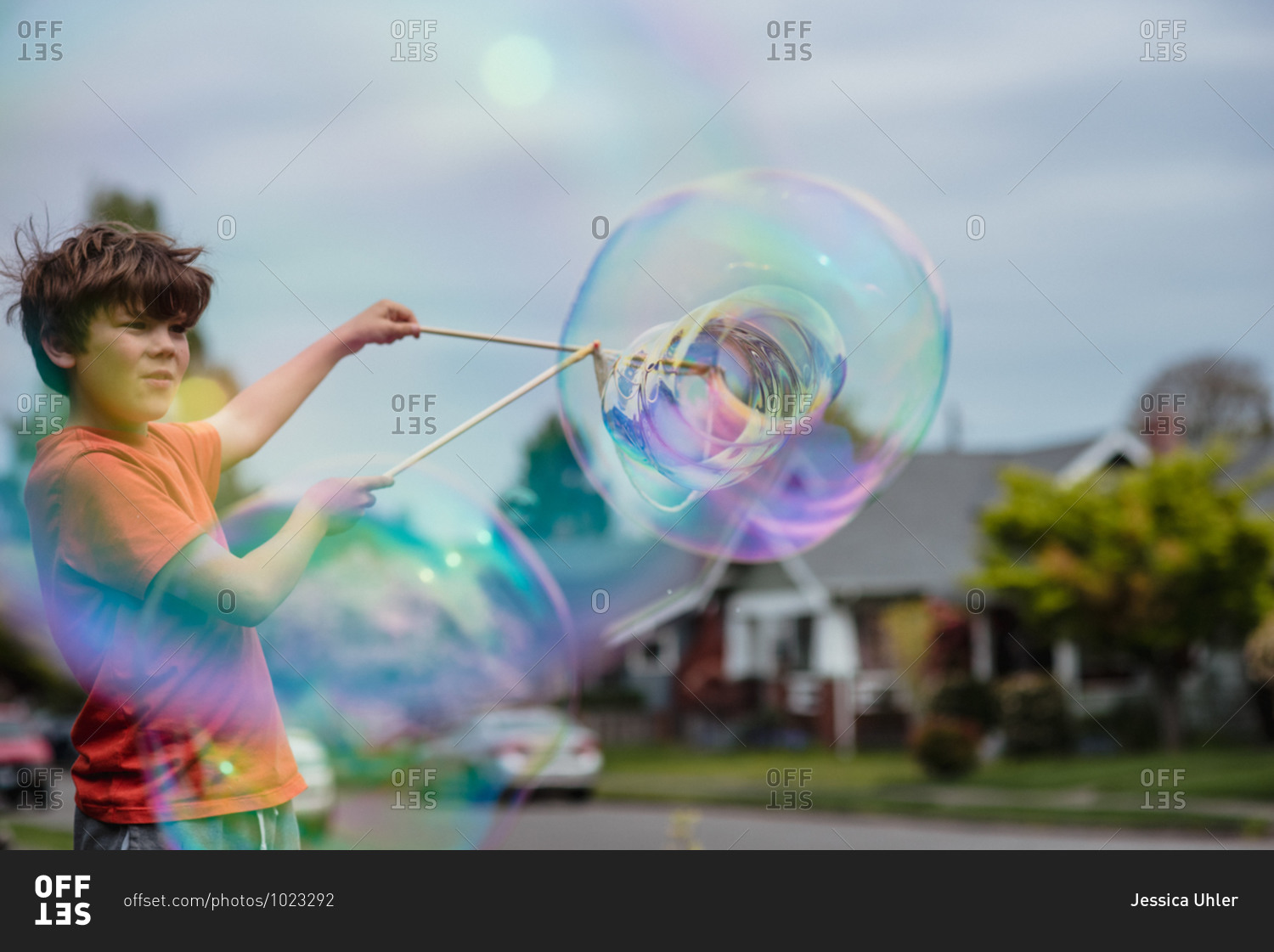 Young boy playing with a large bubble wand in front yard