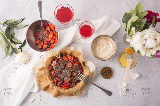 Overhead view of a strawberry galette with vanilla bean and chia seeds being prepared on light surface