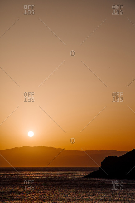Peaceful scenery of sea and mountain range under sky with amazing orange sundown