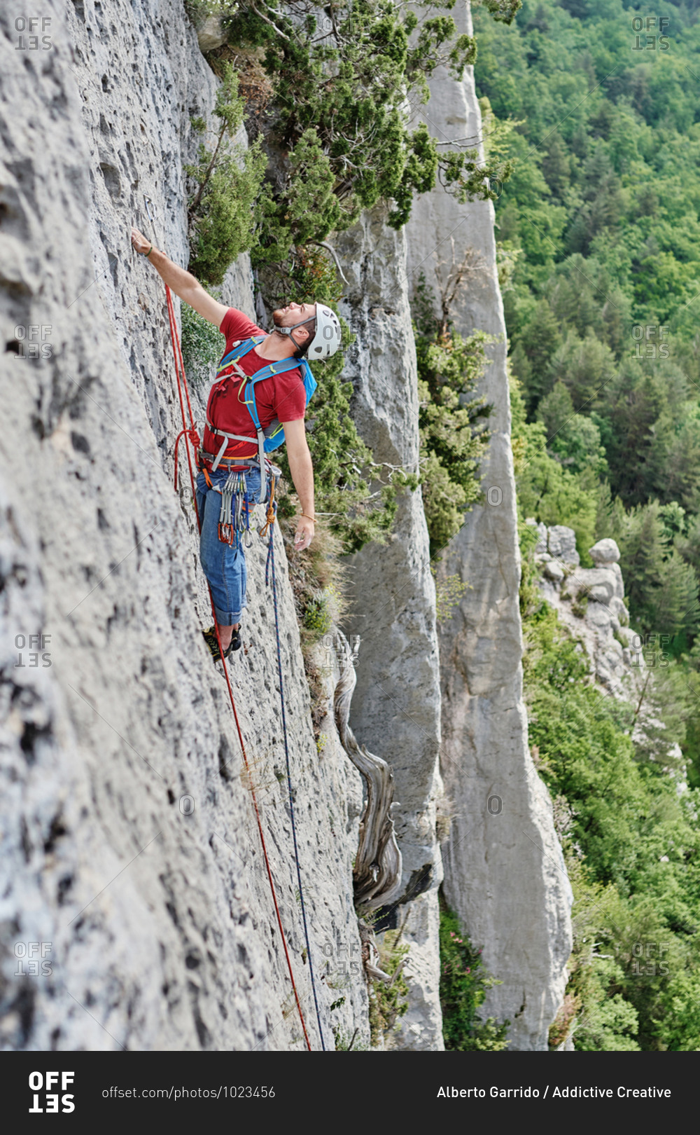 Side view of mountaineer in safety equipment climbing steep rock during summer vacation
