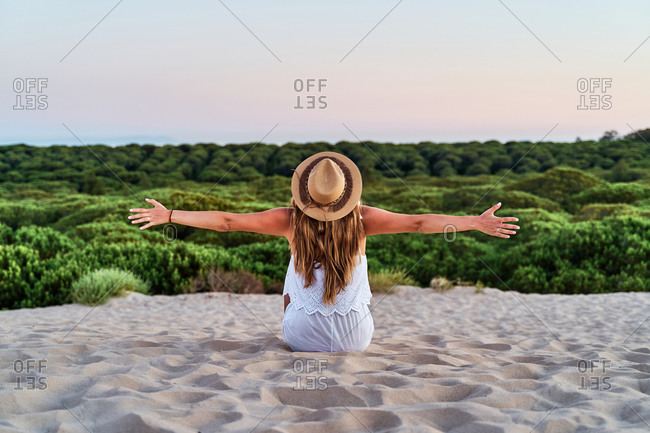 Back view of calm female sitting on beach and admiring wonderful natural landscape during sunset