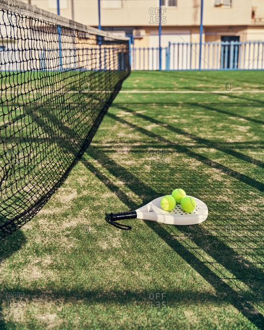 Modern racket and balls for paddle tennis placed on grass of sports ground on sunny day in summer