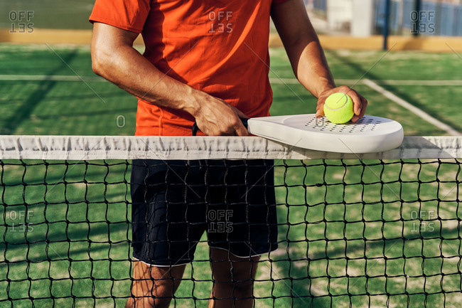 Unrecognizable male player standing on court near net with racket and ball for paddle tennis