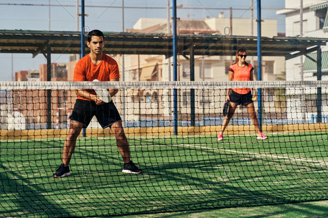 Determined sportsman and sportswoman in activewear playing paddle tennis on sports ground in summer on sunny day