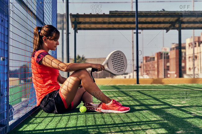 Side view of female player sitting with racket and ball on sports ground for paddle tennis