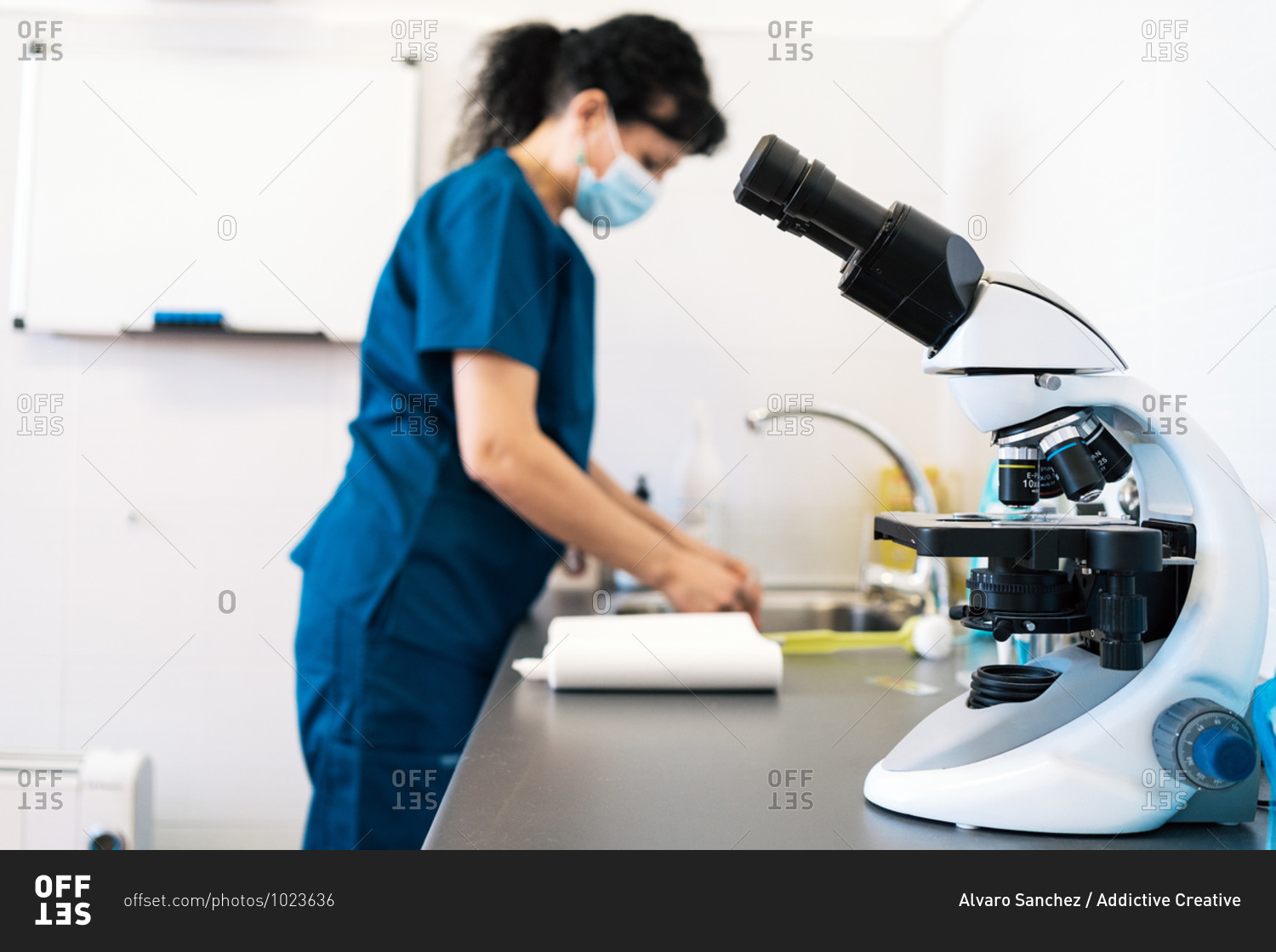 Modern microscope placed on table near female doctor in medical mask in lab of modern clinic
