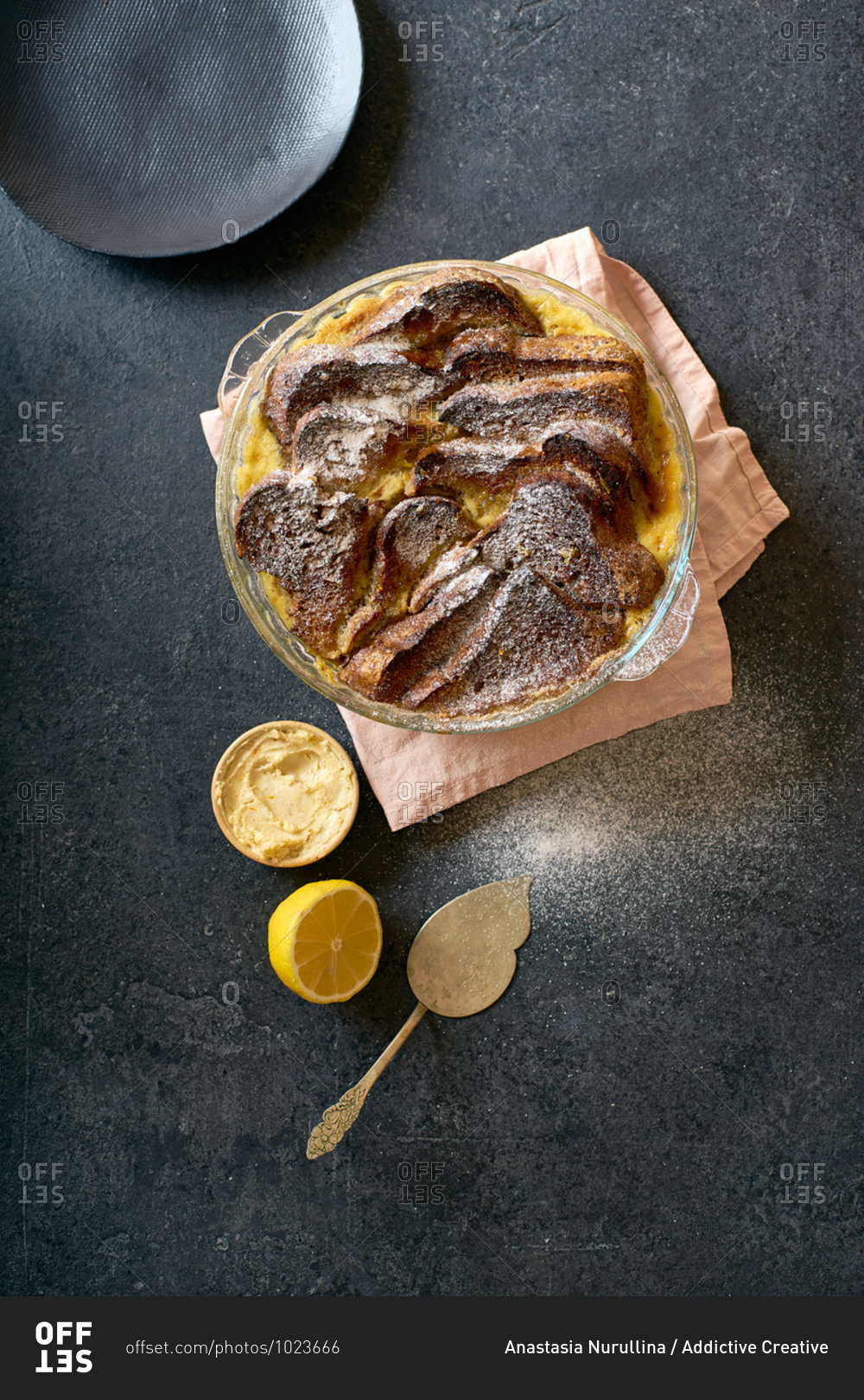Top view of traditional bread pudding with custard, served with aromatic orange zest butter and powdered sugar on dark background