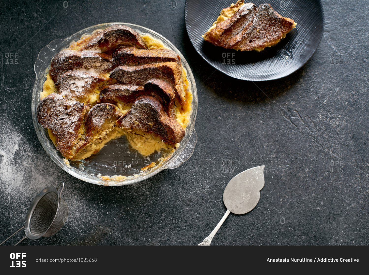 Top view of traditional bread pudding with custard, served with aromatic orange zest butter and powdered sugar on dark background