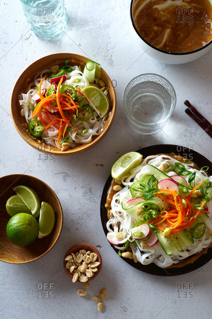 Healthy lunch with vegan rice noodle salad made with fresh vegetables, lime and peanut sauce and a glass of water