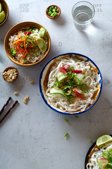Healthy lunch with vegan rice noodle salad made with fresh vegetables, lime and peanut sauce and a glass of water