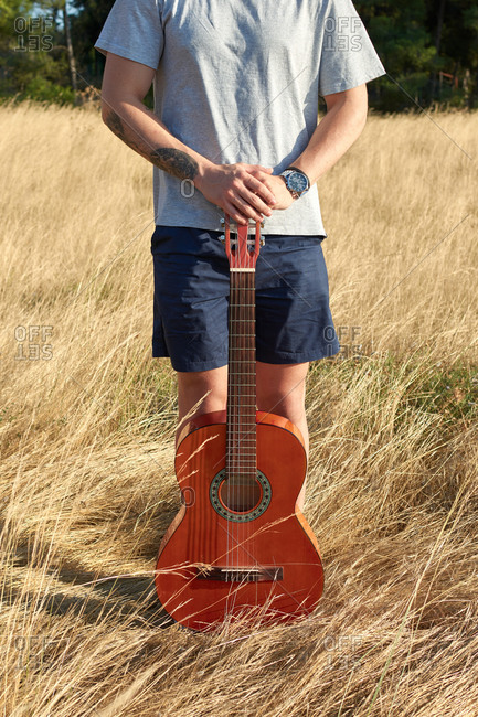 Unrecognizable male musician standing with guitar in dry meadow on sunny day in summer