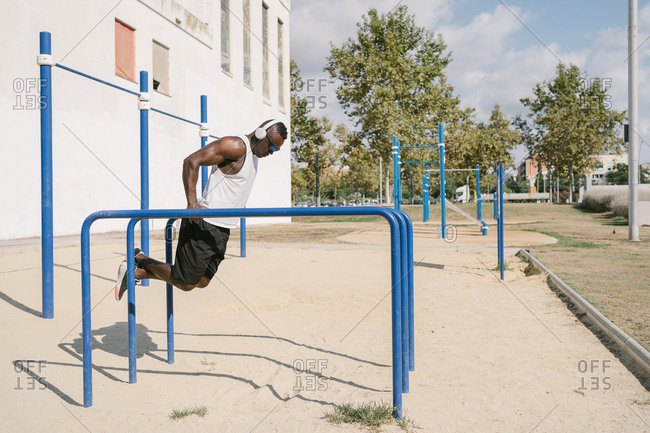 Full length of shirtless athletic African American male doing exercise on fitness equipment while training alone on sports ground