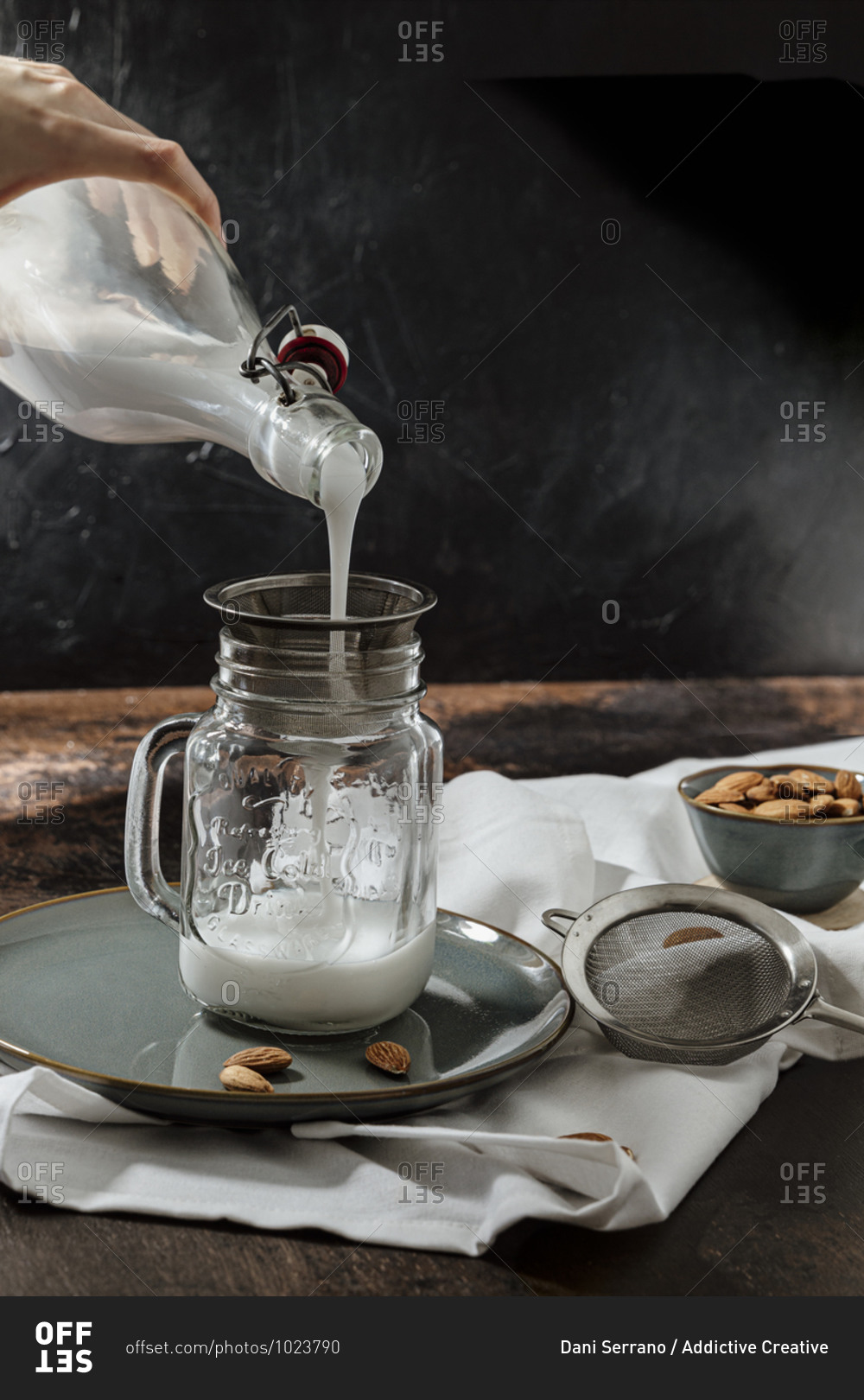 Unrecognizable person filling glass jar with almond milk from bottle on plate and cloth