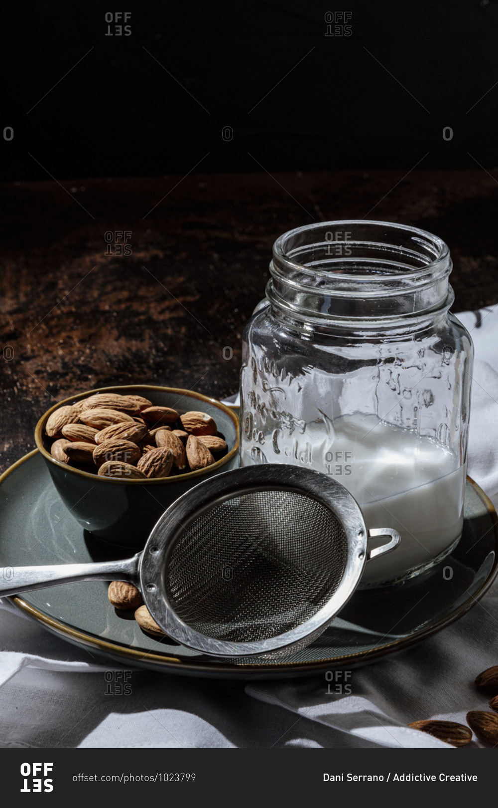 Bowl of natural almonds placed near glass jar of fresh vegan milk on plate and napkin in dark room