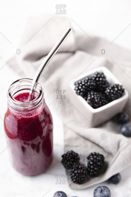 Vertical close up shot of a glass bottle with berry smoothie and a metal straw inside.