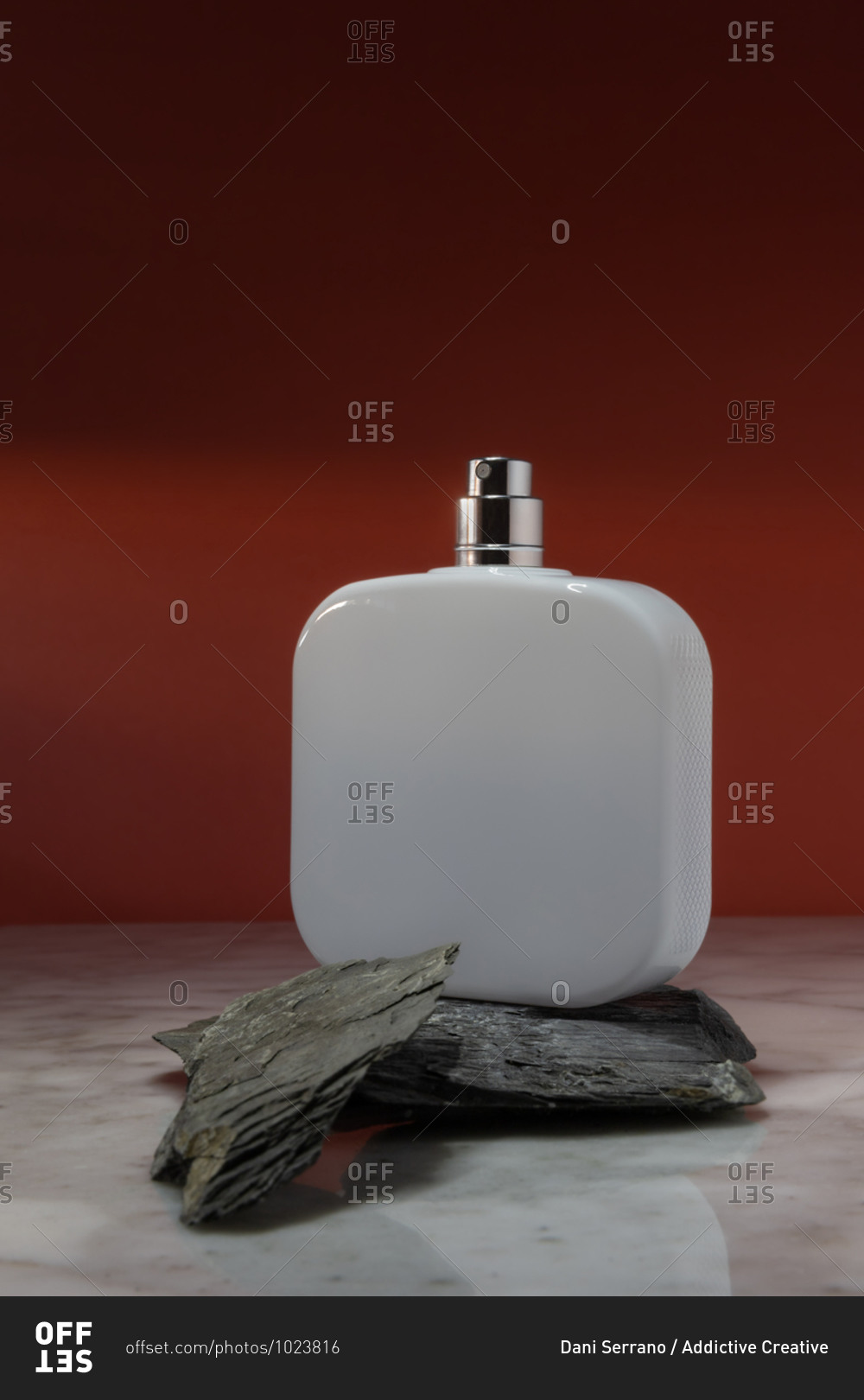 White cosmetic spray bottle arranged on stones on marble surface against red wall