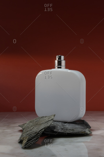 White cosmetic spray bottle arranged on stones on marble surface against red wall