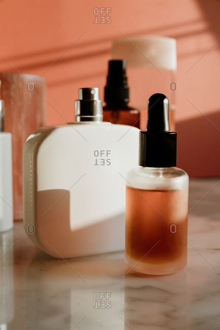 Glass dropper flask with skincare serum placed near spray bottle and other containers with cosmetic products on marble table against pink wall