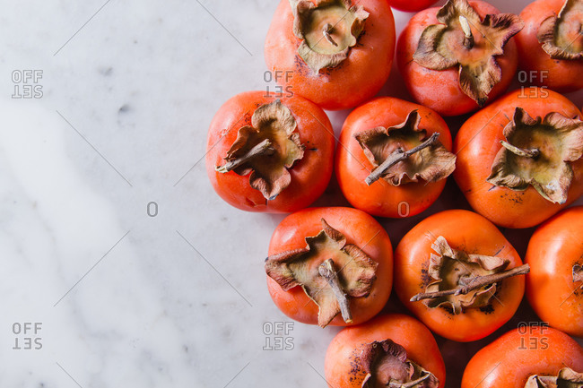 Top view of several ripe persimmons placed on marble table in bright modern kitchen