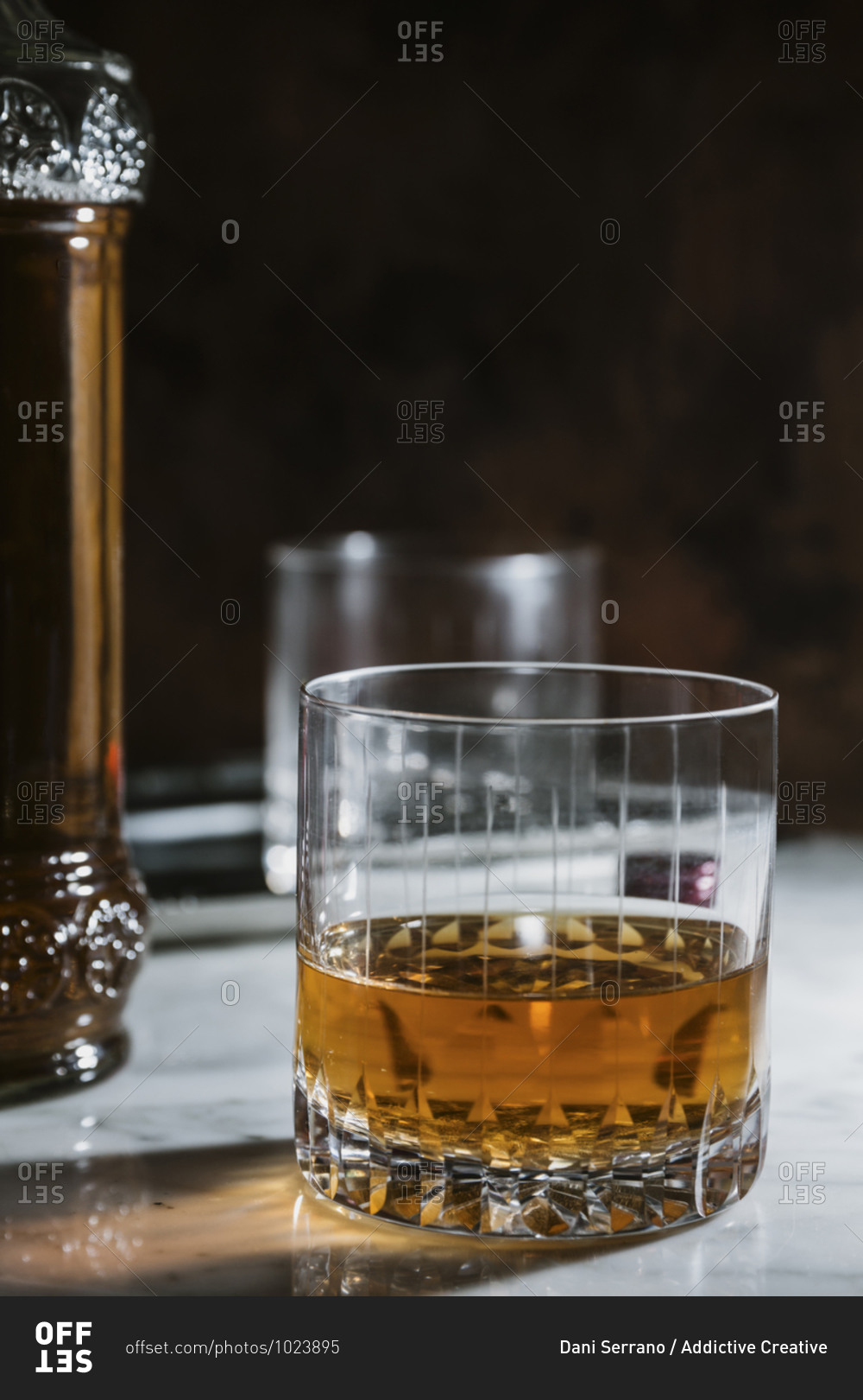 Side view of whiskey in glass and bottle arranged on marble table in bar