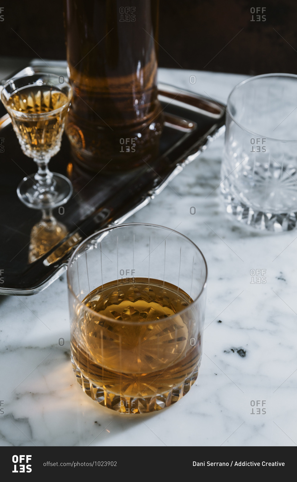 High angle of whiskey in glass and bottle arranged on marble table in bar