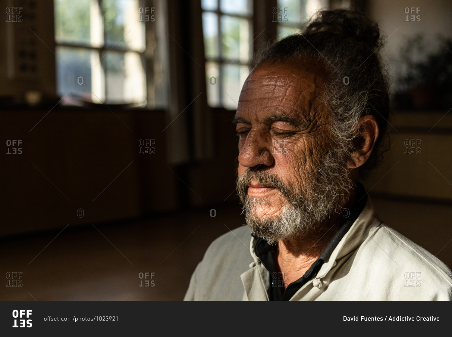Serious elderly bearded ethnic male instructor of traditional chi kung or qigong with closed eyes while standing in dark room