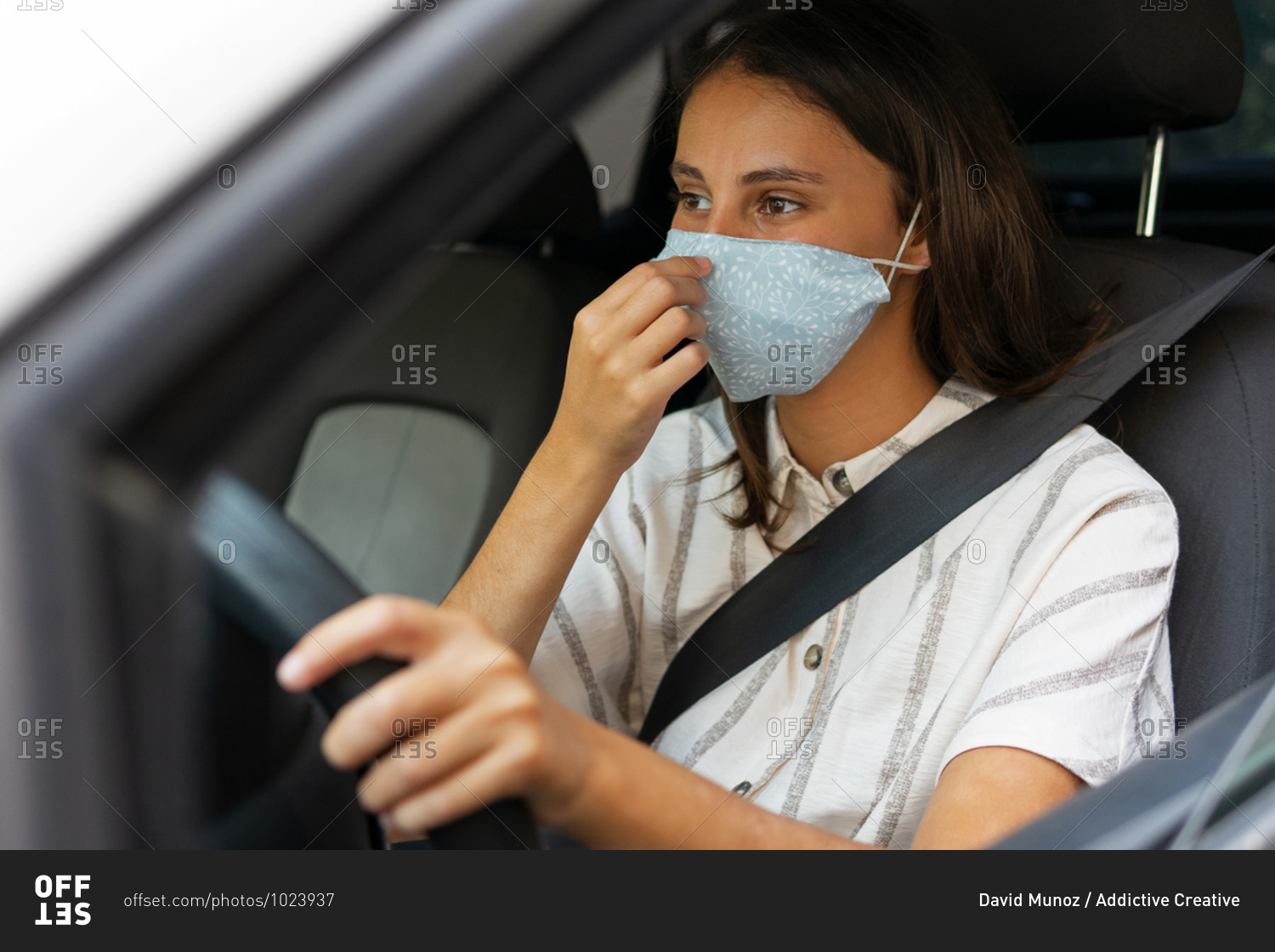 Content female driver in medical mask driving automobile in city during coronavirus epidemic