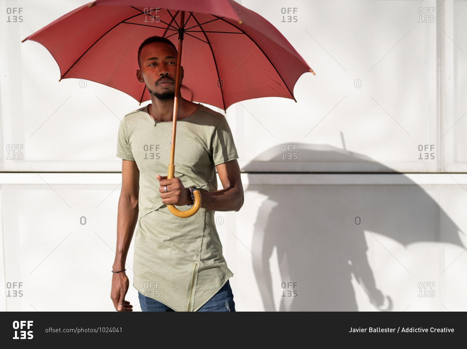 Tranquil black male standing under umbrella in city looking away and enjoying sunny weather in summer