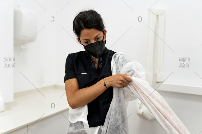 Female medical specialist putting on protective suit with face mask while preparing for work during coronavirus pandemic