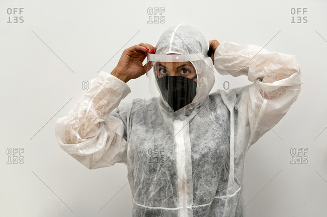 Female medical specialist putting on protective suit with face mask and protective cap while preparing for work during coronavirus pandemic