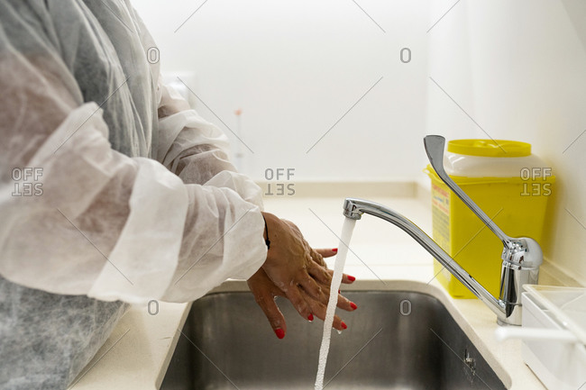 Side view of female doctor in protective suit washing hands while preparing for medical procedure in modern clinic