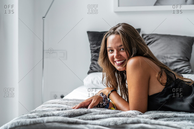 Side view of charming female in nightwear lying on soft bed in morning and looking at camera