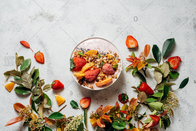 Top view of nutritious smoothie bowl with strawberries and nuts arranged on table with green plant and various fruits