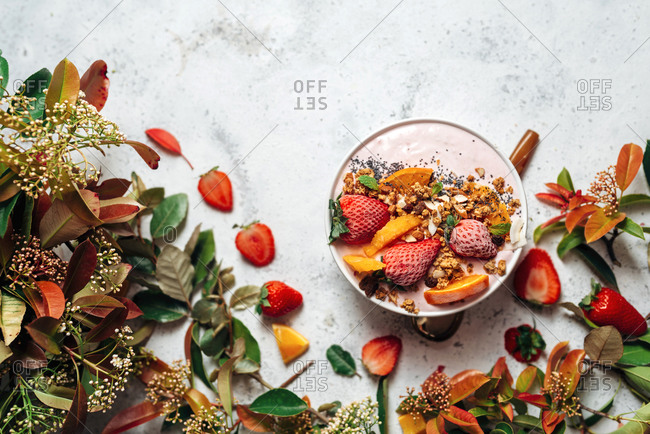 Top view of nutritious smoothie bowl with strawberries and nuts arranged on table with green plant and various fruits