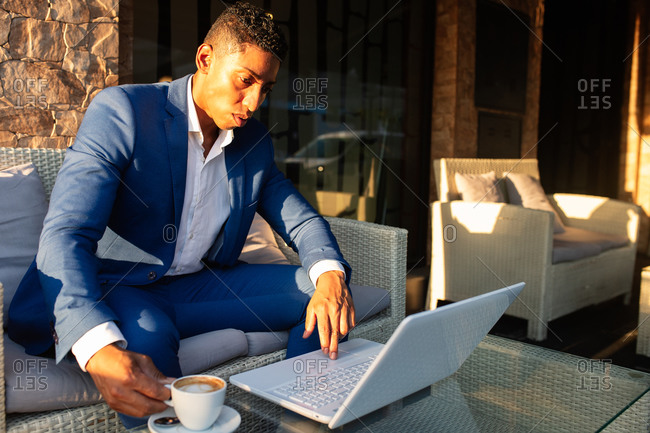 Young African American male entrepreneur in formal wear working on laptop and thinking about financial problem while sitting in lounge zone of modern cafeteria